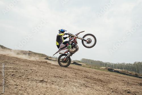 Fotografía Motorcyclist jumping and riding on rear wheel at enduro motocross training groun