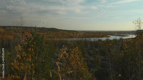 Morning landscape shot in time laps. Calm waters of a quiet flat river flow through a wide valley. Red autumn birch forest around. The low morning sun illuminates the landscape.