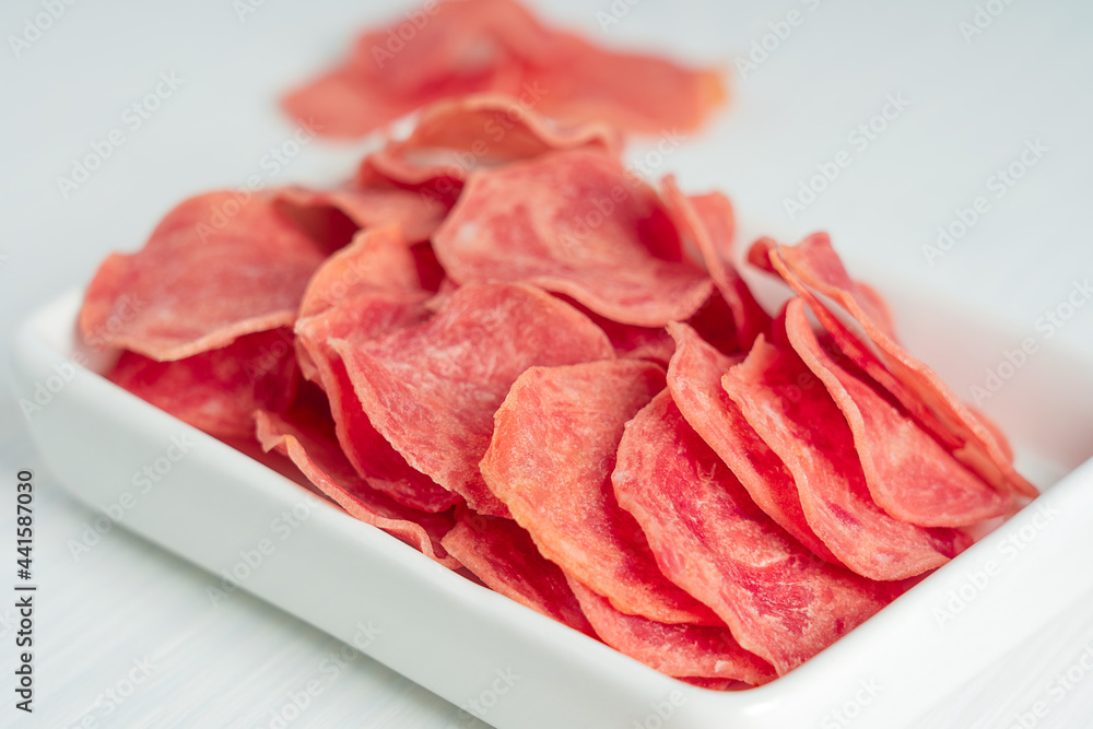 Closeup view of salted slices of jerky pork or beef organic tasty meat dehydrated or dried full of protein served as healthy snack or appetizer in plate on white wooden background. Horizontal Closeup view of salted slices of jerky pork or beef organic tasty meat dehydrated or dried full of protein served as healthy snack or appetizer in plate on white wooden background. Horizontal