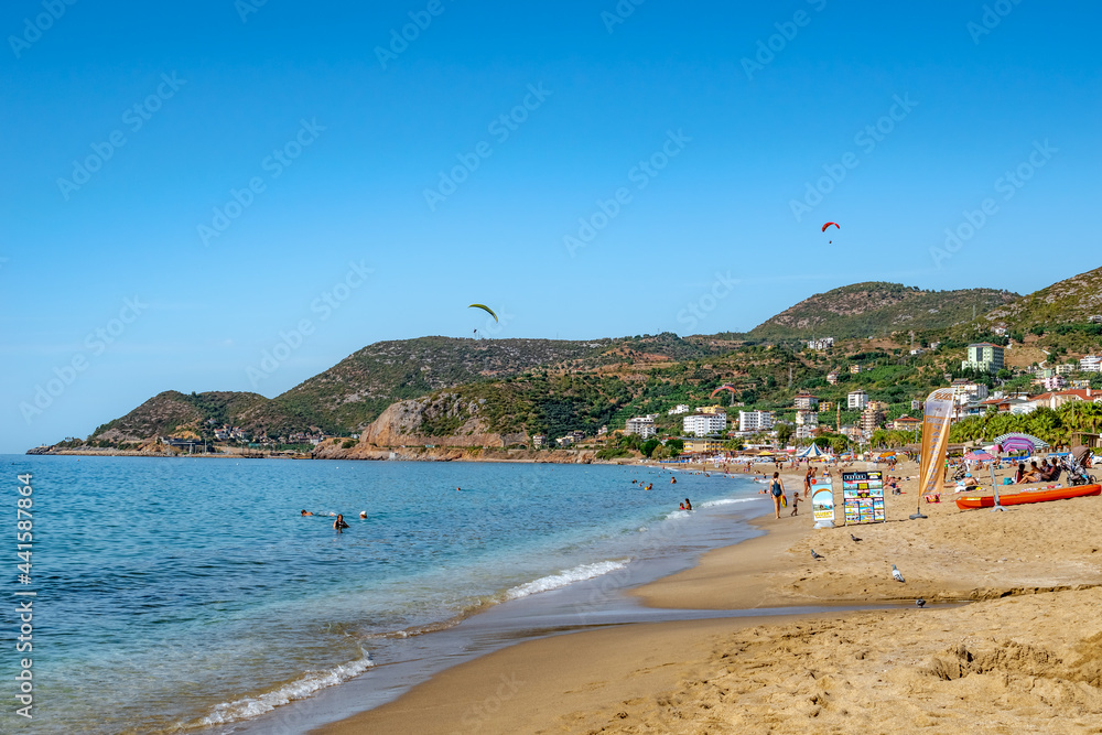 Alanya, Turkey - October 23, 2020: Beautiful summer-autumn view of Kleopatra beach in Alanya. Coastline with clean yellow sand, blue-turquoise water and people resting on the backdrop of mountains