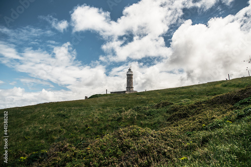 Lighthouse on grassy hill under cloudy sky