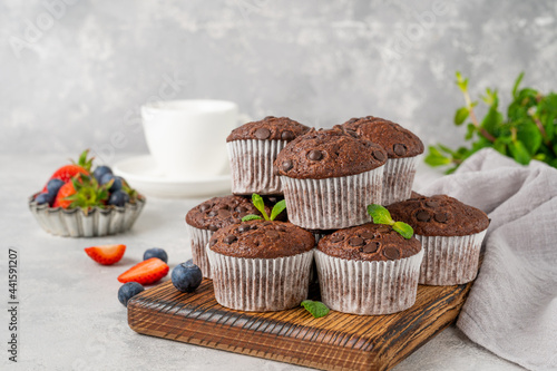 Fototapeta Naklejka Na Ścianę i Meble -  Chocolate muffins or cupcakes with chocolate drops on a wooden board on a gray background with fresh berries and mint. Copy space.