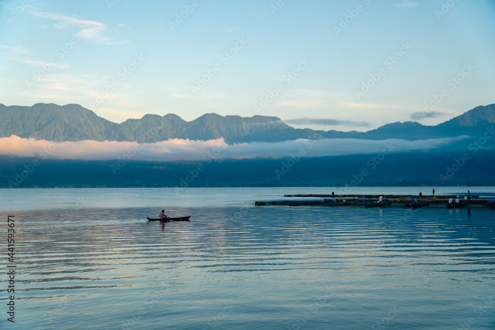 Beautiful panoramic view of Lake Maninjau, West Sumatra, Indonesia in blue hour of the morning, with a small fishing boat sailing. Beautiful nature landscape of Indonesia.