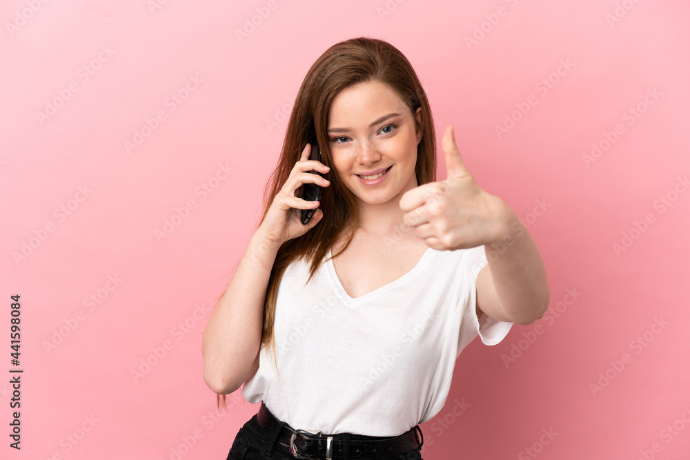 Teenager girl over isolated pink background keeping a conversation with the mobile while doing thumbs up Teenager girl over isolated pink background keeping a conversation with the mobile while doing thumbs up