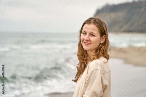 Girl on the beach have fun. Caucasian beautiful woman is happy on the beach against the background of the sea. Beige clothes and sand in the fall.