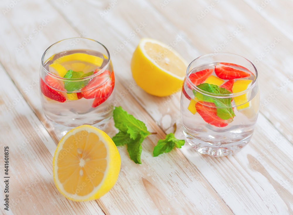 Fototapeta premium two glasses of lemon, strawberry and mint drink and lemon halves on the table. homemade summer refreshing drink.