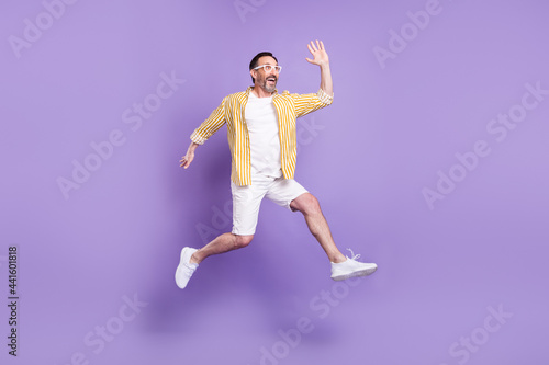 Photo of impressed friendly mature man dressed shirt glasses jumping waving arm empty space isolated purple color background