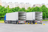 Two trucks in a parking lot with an empty container trailer open gates at the back, ready to load products, goods cargo.