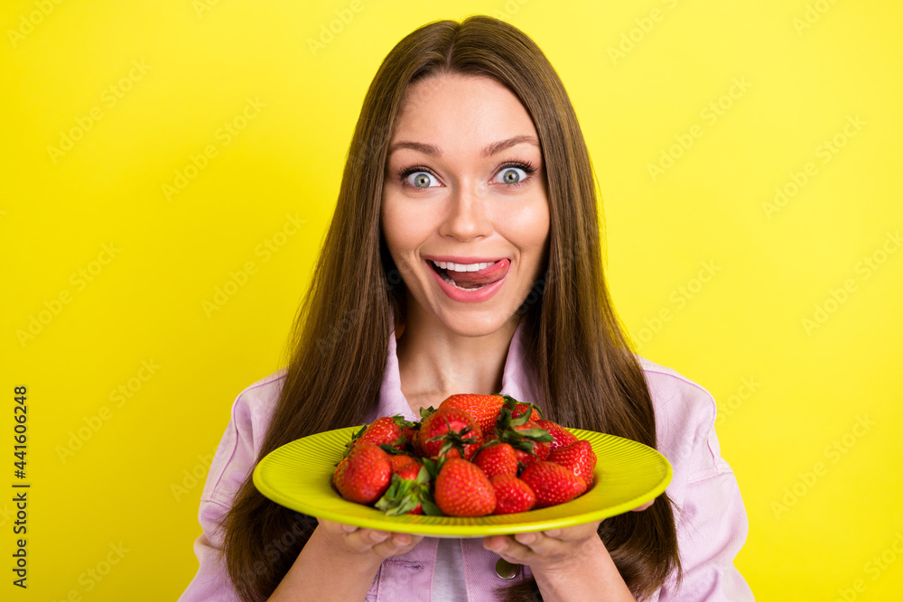 Photo portrait young woman keeping plate with strawberries smiling licking lips hungry isolated vibrant yellow color background Photo portrait young woman keeping plate with strawberries smiling licking lips hungry isolated vibrant yellow color background