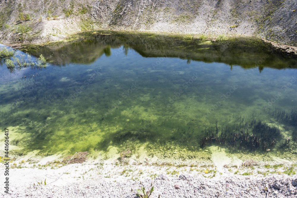 clear blue water in an abandoned chalk quarry with steep banks overgrown with grass and bushes landscape
