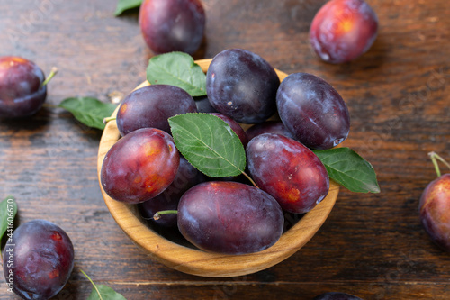 Fresh plums with leaves in a wooden bowl on a brown table.