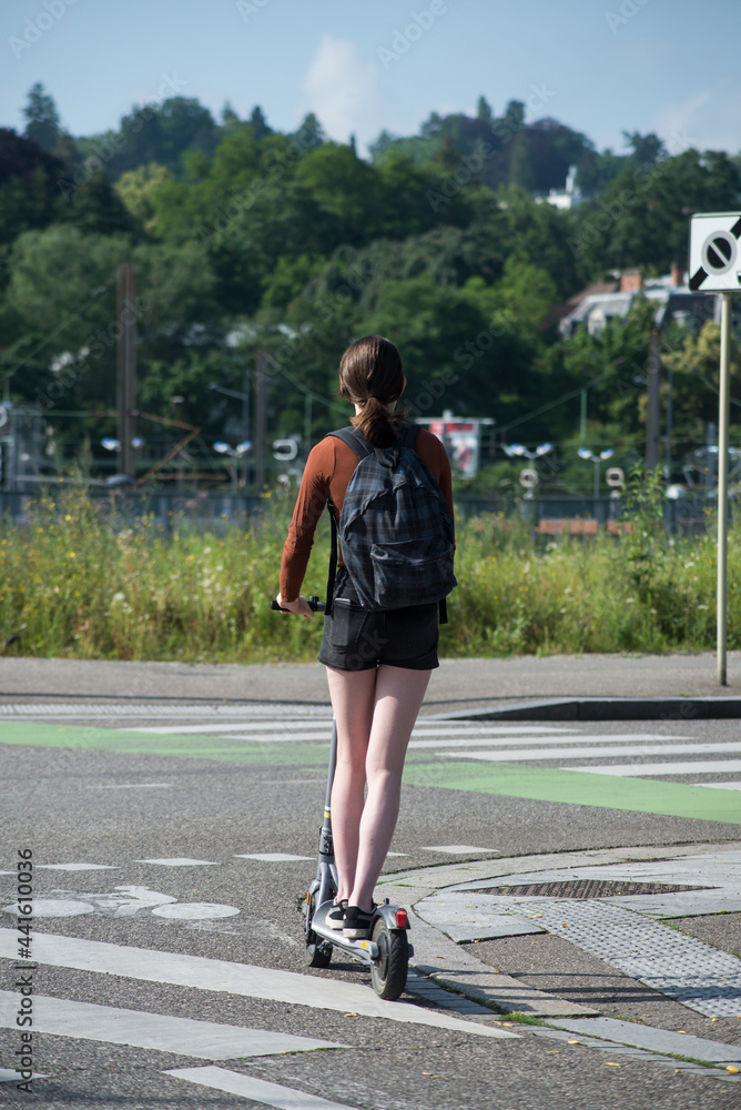 Portrait on back view of girl standing on electric scooter in the street