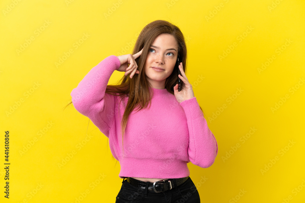 Teenager girl using mobile phone over isolated yellow background having doubts and thinking Teenager girl using mobile phone over isolated yellow background having doubts and thinking