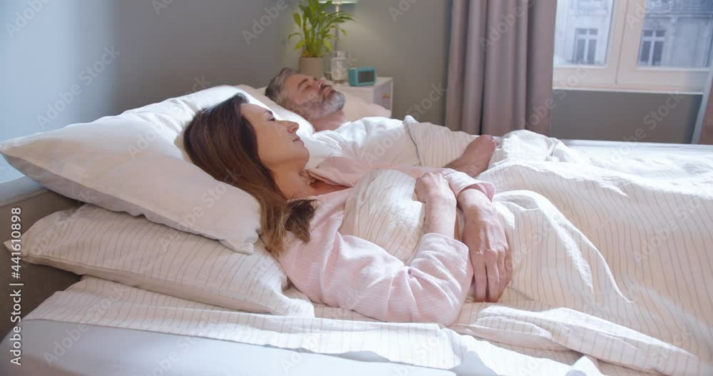 Portrait of woman blocking ears with the pillow while man snoring on bed. Adult unhappy woman can't sleep because her man is snoring at the bed. Problems with breathing concept Portrait of woman blocking ears with the pillow while man snoring on bed. Adult unhappy woman can't sleep because her man is snoring at the bed. Problems with breathing concept