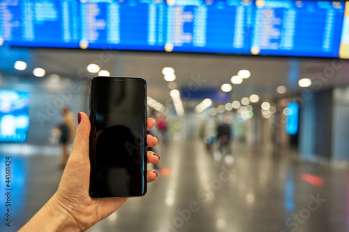 Smartphone in hand against the background of the information board at the airport