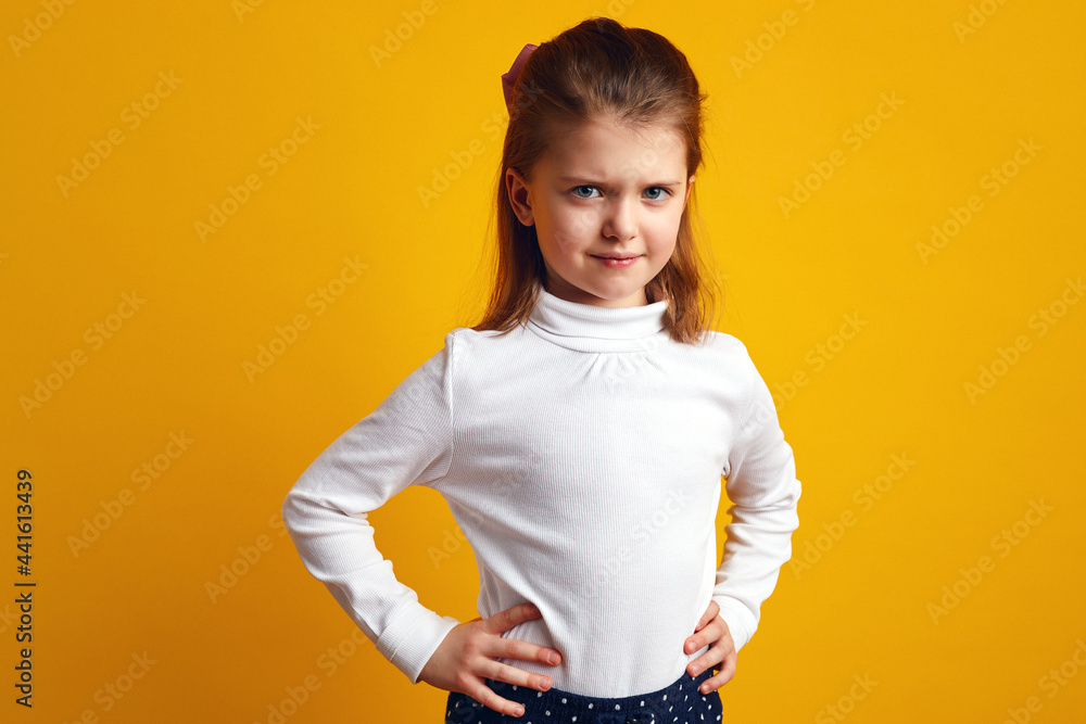 Displeased young girl frowning face and keeping hands on waist over yellow Displeased young girl frowning face and keeping hands on waist over yellow