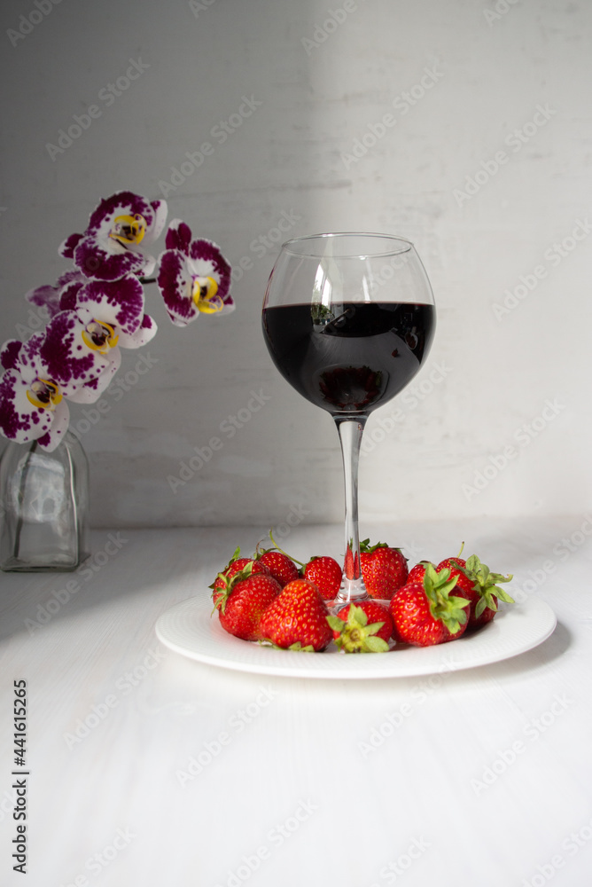 Red strawberries on plate with wine glass on white background and orchid flower in vase Red strawberries on plate with wine glass on white background and orchid flower in vase