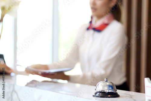 Closeup of silver bell ring on hotel reception service desk with receptionist service customer at hotel counter desk as blurred background.