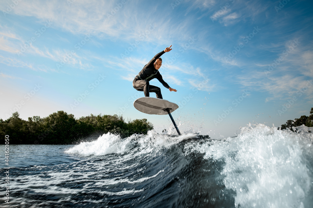athletic man balancing on foilboard on wave on sunny day