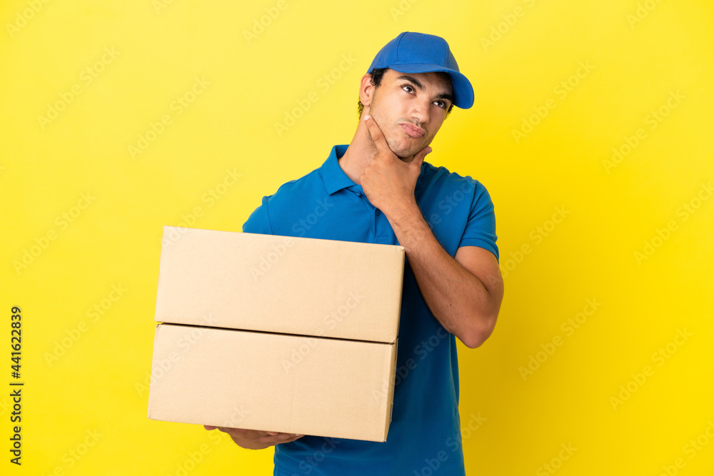 Delivery man over isolated yellow wall having doubts Delivery man over isolated yellow wall having doubts