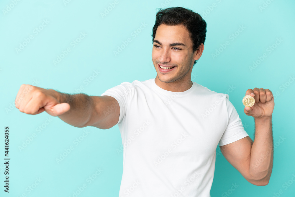 Young man holding a Bitcoin over isolated blue background giving a thumbs up gesture Young man holding a Bitcoin over isolated blue background giving a thumbs up gesture