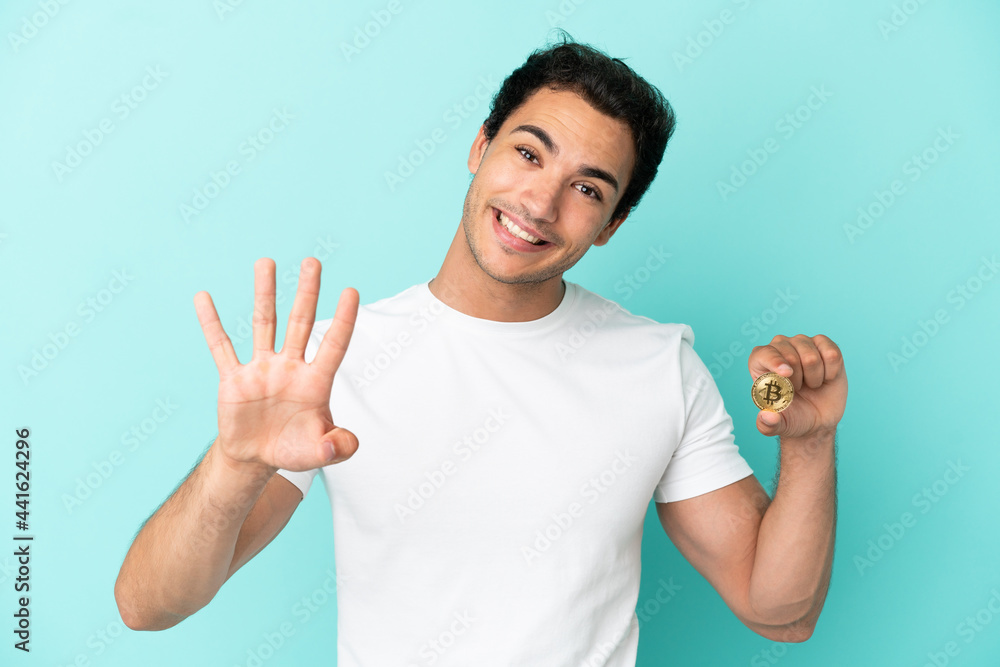 Young man holding a Bitcoin over isolated blue background happy and counting four with fingers Young man holding a Bitcoin over isolated blue background happy and counting four with fingers