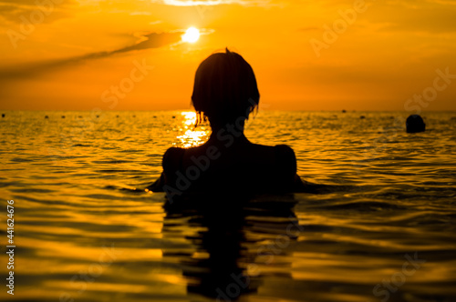 Girl swimming in the sea at sunset, splashes of transparency water, female black silhouette © Wingedbull