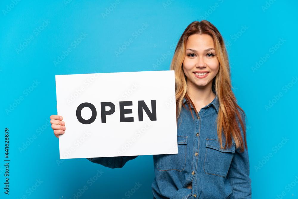 Teenager girl over isolated blue background holding a placard with text OPEN with happy expression