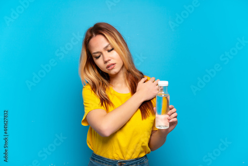 Teenager girl with a bottle of water over isolated blue background suffering from pain in shoulder for having made an effort
