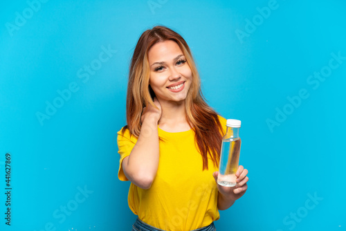 Teenager girl with a bottle of water over isolated blue background laughing