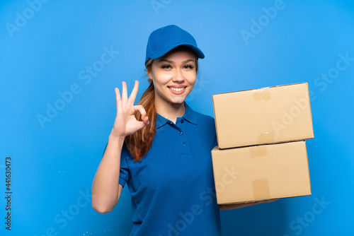 Delivery girl over isolated blue wall showing ok sign with fingers photo