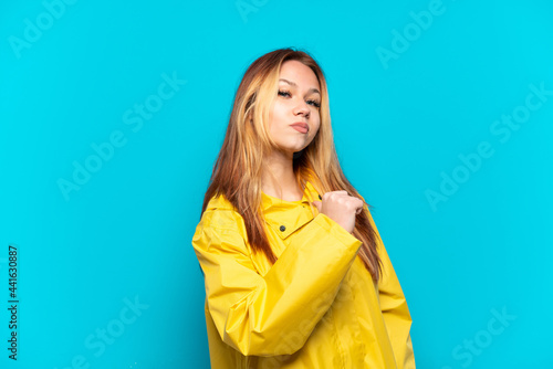 Teenager girl wearing a rainproof coat over isolated blue background proud and self-satisfied