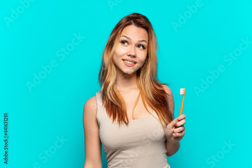 Teenager girl brushing teeth over isolated blue background thinking an idea while looking up