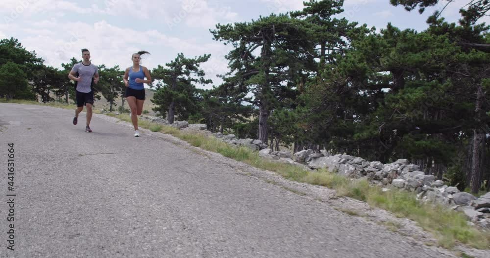 Tracking slow motion shot of sportive couple jogging outdoors in the morning, trail running experience in nature. Healthy lifestyle concept. Tracking slow motion shot of sportive couple jogging outdoors in the morning, trail running experience in nature. Healthy lifestyle concept.