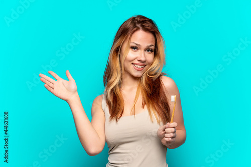 Teenager girl brushing teeth over isolated blue background extending hands to the side for inviting to come