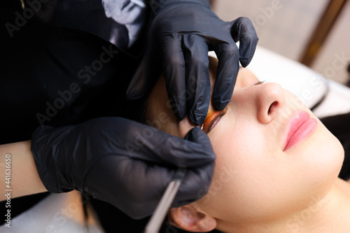 the hands of the master close - up apply a special roller for curling cilia to the client's eyelid