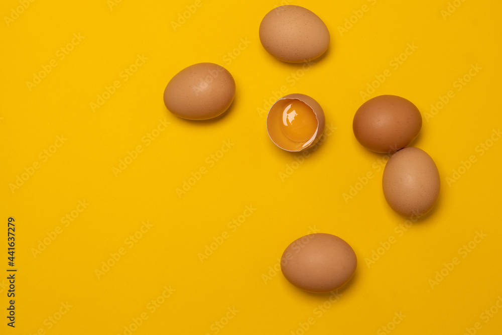 Organic brown chicken eggs and one broken egg with yolk on a yellow background Organic brown chicken eggs and one broken egg with yolk on a yellow background