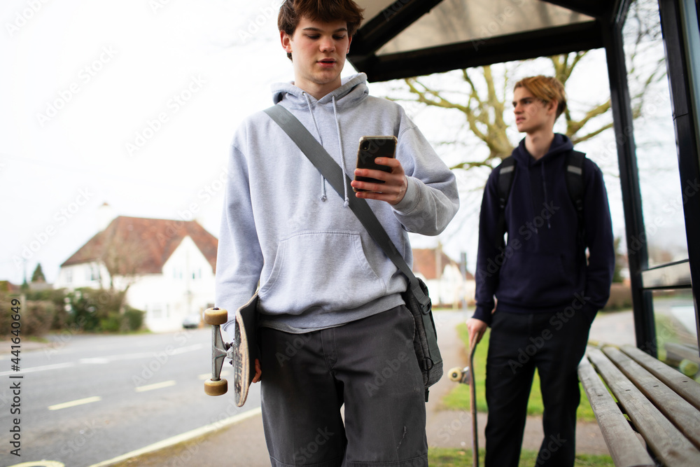 Teenage boys with skateboards and smart phone at bus stop Teenage boys with skateboards and smart phone at bus stop