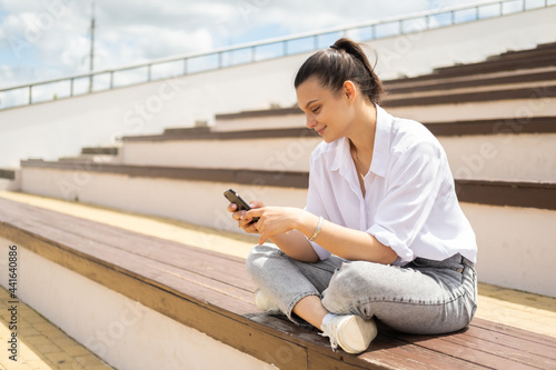 Happy cheerful young women with smartphone enjoying sunny day sitting in amphitheater