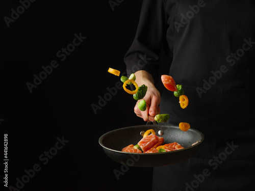 Red fish and vegetables in a pan in a state of levitation. Black background. Focusing on the foreground. Contrasting colors.Color image.