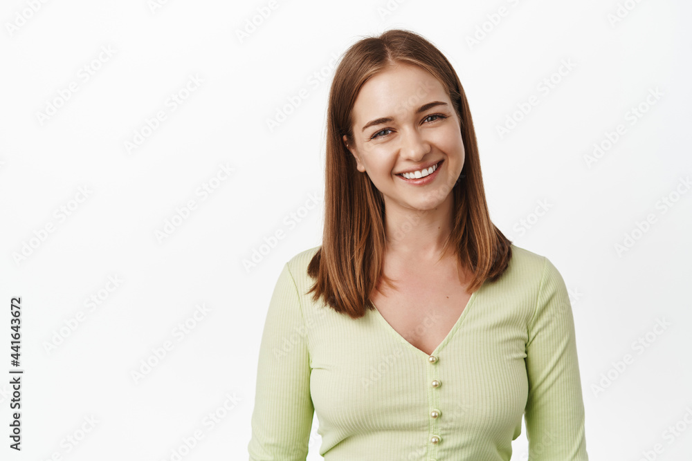 Close up of young pleasant girl, smiling and looking friendly, happy cute face expression, smile white teeth, standing in casual blouse against white background Close up of young pleasant girl, smiling and looking friendly, happy cute face expression, smile white teeth, standing in casual blouse against white background