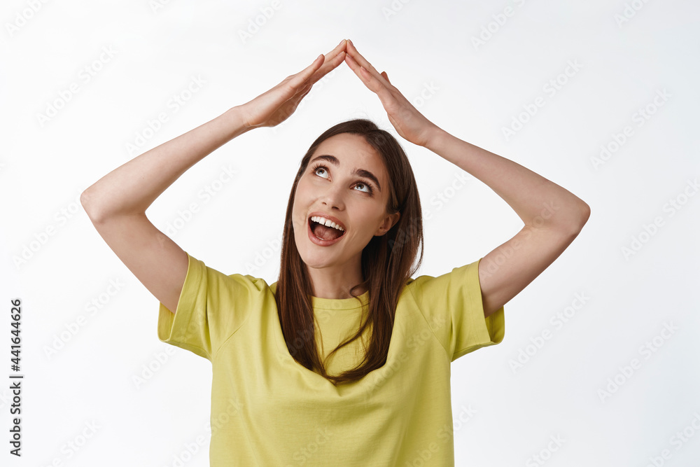 Close up portrait of excited smiling girl building roof house with hands above head, feel secured, looking happy at rooftop, standing over white background