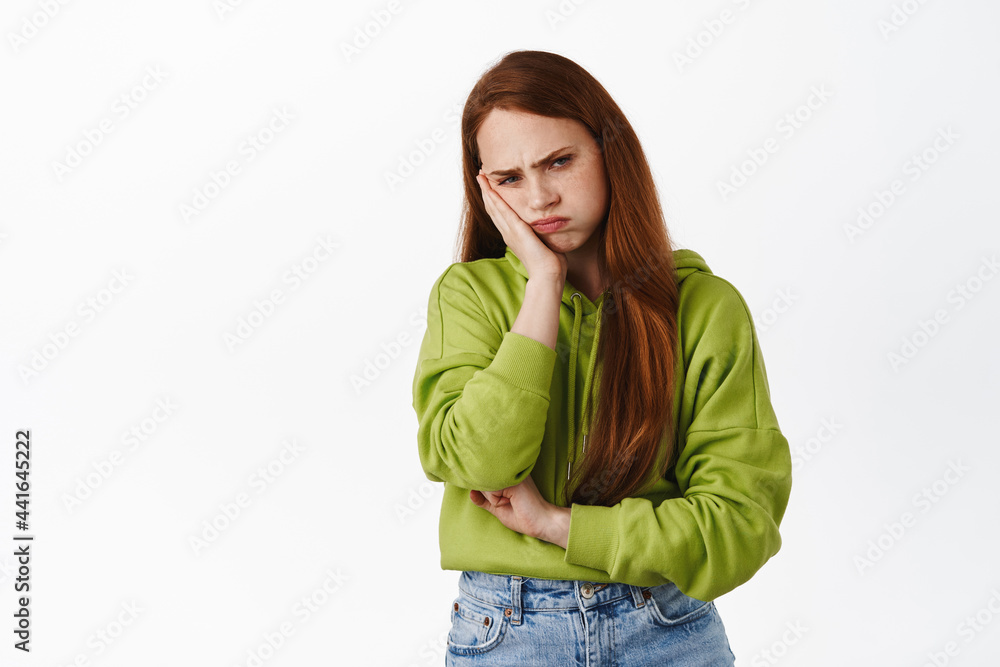 Annoyed teen redhead girl sulking, looking bothered and upset, pouting at folks, lean on hand and frowning displeased, standing angry against white background Annoyed teen redhead girl sulking, looking bothered and upset, pouting at folks, lean on hand and frowning displeased, standing angry against white background