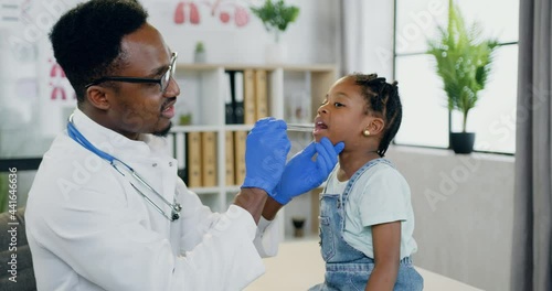 Lovely small black girl sitting near handsome caring african american male doctor which examining her throat and mouth with spatula,pediatry concept photo