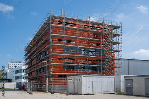 construction site of a red brick building with scaffolding at the outside at a sunny day