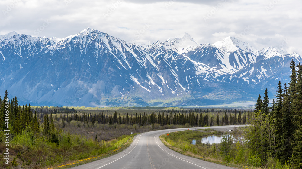 Huge snow capped mountain scene seen outside of Haines Junction, Yukon Territory, Canada with winding road heading to road trip, awe inspriring mountains in spring time. Huge snow capped mountain scene seen outside of Haines Junction, Yukon Territory, Canada with winding road heading to road trip, awe inspriring mountains in spring time.