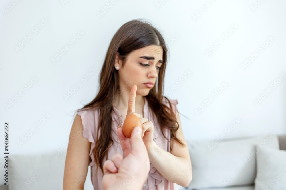 Selective focus of a beautiful young women refusing to eat eggs. Young beautiful woman holding fresh egg at home with open hand doing stop sign with serious and confident expression. Selective focus of a beautiful young women refusing to eat eggs. Young beautiful woman holding fresh egg at home with open hand doing stop sign with serious and confident expression.