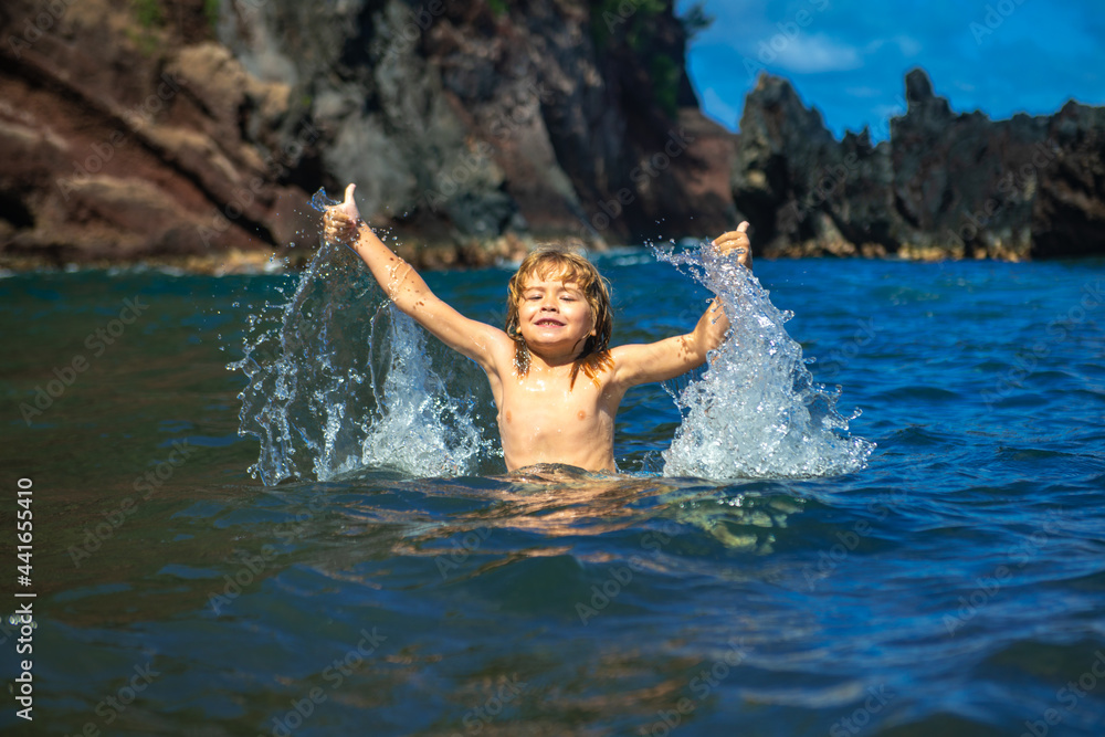 Amazed child playing and splashing in the sea. Kid having fun outdoors. Summer vacation and healthy family lifestyle concept. Little boy raises hands up in the water and splashes water drops.