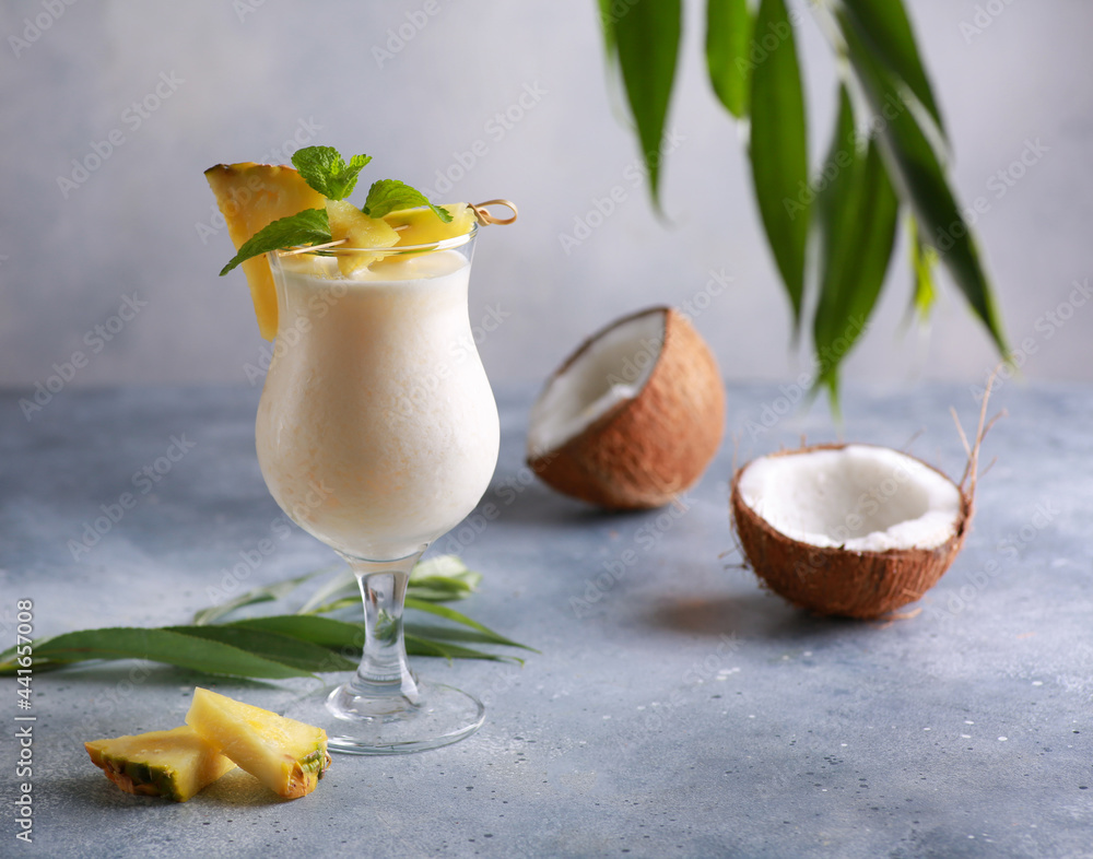 Summer. Drinks and cocktails. Pina colada in glass with pineapple, coconut, mint and a branch of greenery on a light gray background. Background image, copy space - obrazy, fototapety, plakaty 