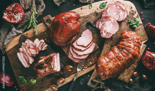 Foto Assortment of cold meats products, ham, sausage, salami, parma, prosciutto, bacon on wooden cutting board with herb and spices over dark background